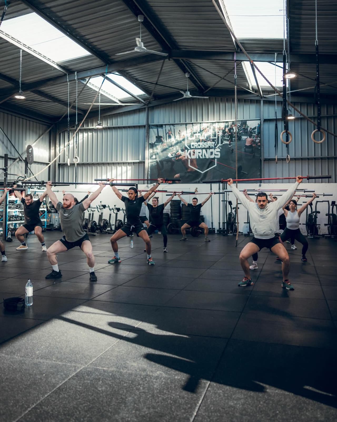 Cours collectif CrossFit Kurnos, squats barre, miroir Kurnos en fond